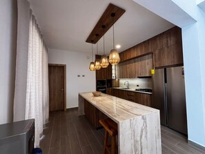 A modern kitchen with a marble island, wooden cabinets, and pendant lighting. - Brand-New 4-Bedroom Villa with Private Pool, SOV (Sosua)