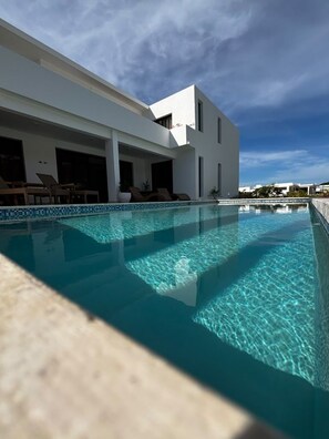 A swimming pool with clear water, a modern building with white walls and balconies, and a clear sky. - Brand-New 4-Bedroom Villa with Private Pool, SOV (Sosua)
