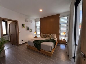 Een moderne slaapkamer met een groot bed, een houten hoofdbord en uitzicht op het landschap door grote ramen.