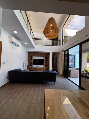 A modern living room with a sectional sofa, a flat-screen TV, and a large window. - Brand-New 4-Bedroom Villa with Private Pool, SOV (Sosua)