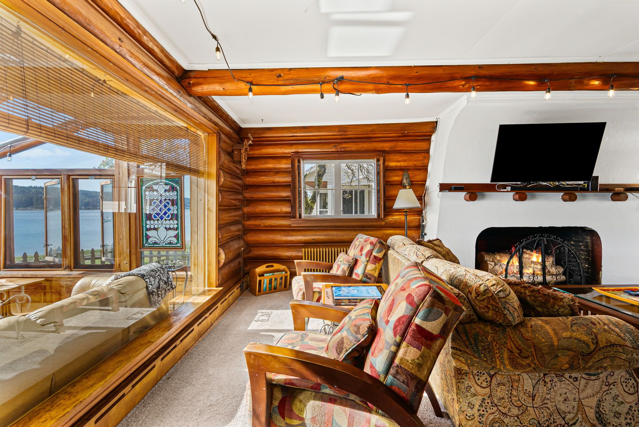 A log cabin interior with a fireplace, wooden walls, a sofa set, and a view of a lake.