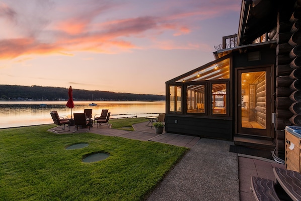 Una cabaña junto al lago con un patio, sillas y una sombrilla roja.