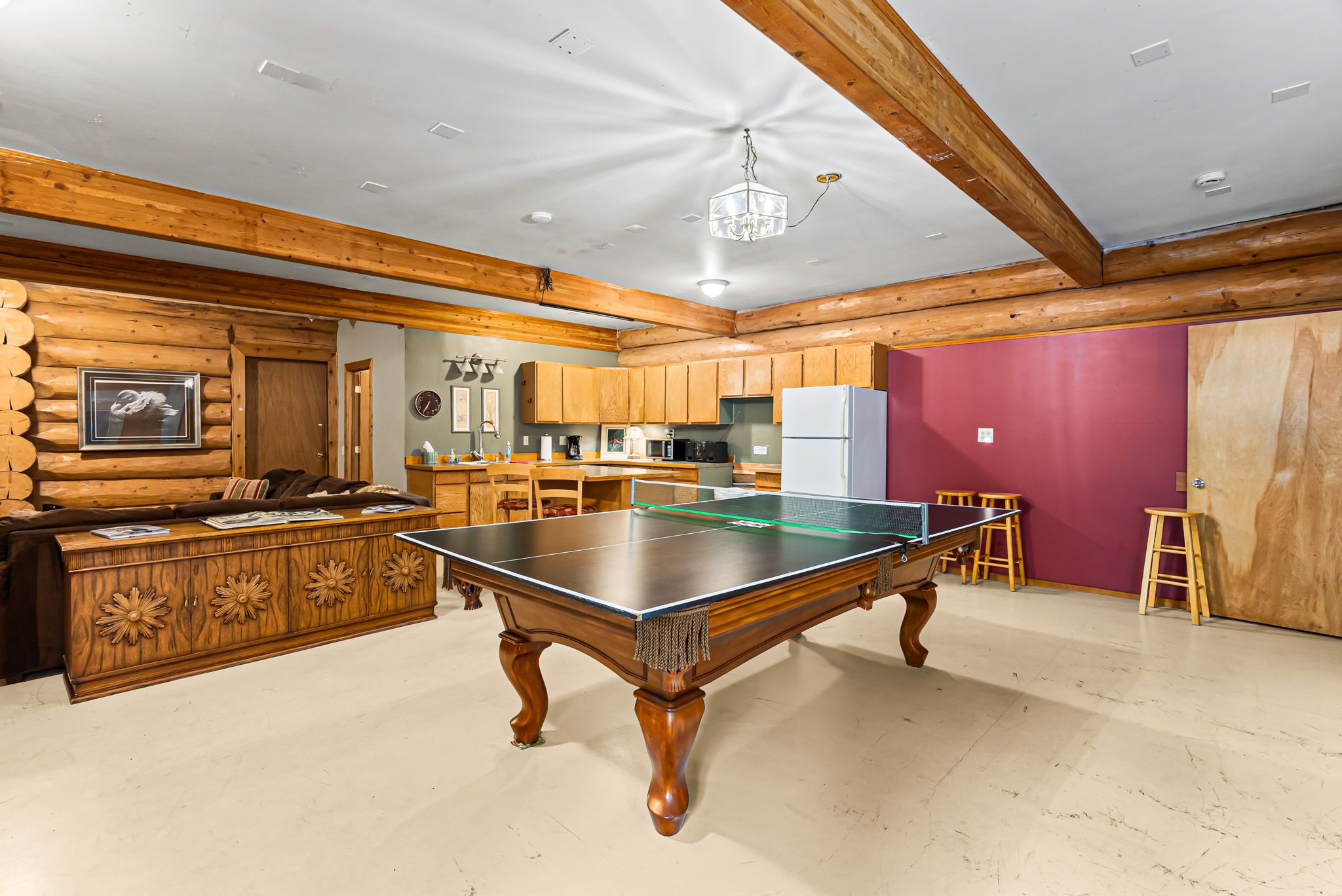A spacious room with a ping pong table, wooden cabinets, a kitchen area, and a wooden ceiling.