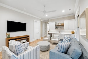 A modern living room with a flat-screen TV, a fireplace, striped sofas, and a round coffee table. - Premier New Build • Spacious 5BR Near Rosemary • Lagoon Pool & Beach Access (Seacrest Beach)