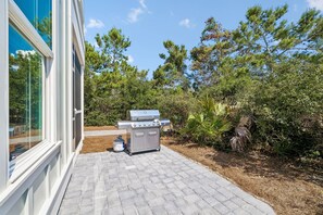 A barbecue grill with a gas tank and a cart, located on a paved patio with a view of a house and surrounding trees. - Premier New Build • Spacious 5BR Near Rosemary • Lagoon Pool & Beach Access (Seacrest Beach)