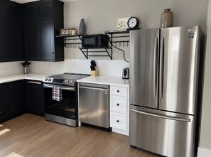 A modern kitchen with black cabinets, a stainless steel refrigerator, a built-in oven, and a microwave on a black shelf. - Serenity on Sherwood | Old Town, Dogs Welcome (Fort Collins)