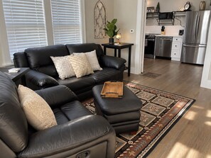 A modern living room with a black leather sectional sofa, a small wooden side table, and a patterned rug. - Serenity on Sherwood | Old Town, Dogs Welcome (Fort Collins)