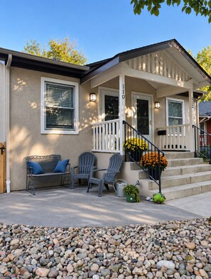 A residential house with a porch, two Adirondack chairs, a bench, and a small garden with flowers. - Serenity on Sherwood | Old Town, Dogs Welcome (Fort Collins)