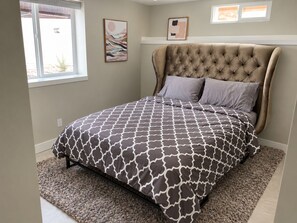 A bedroom with a tufted headboard, a patterned bedspread, and a window with a view. - Solace on Sherwood | Old Town Duplex, Dogs Welcome (Fort Collins)