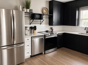 A modern kitchen with stainless steel appliances, black cabinetry, and a wooden floor. - Solace on Sherwood | Old Town Duplex, Dogs Welcome (Fort Collins)