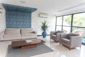 Uma sala de estar moderna com um sofá, duas poltronas, uma mesa de centro e uma grande janela com vista para o verde.
