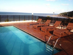 Piscina com espreguiçadeiras e vista para o mar.