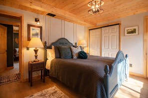 A bedroom with a wooden ceiling, a bed with a headboard, two bedside lamps, a door, and a framed picture on the wall. - Luxury Cabin with EV Tesla Charger & Hot Tub! (Idyllwild-Pine Cove)