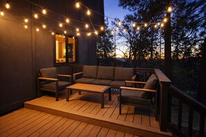 An outdoor deck with a sofa and chairs, string lights, and a view of trees. - Luxury Cabin with EV Tesla Charger & Hot Tub! (Idyllwild-Pine Cove)