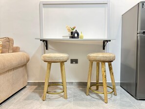 A kitchenette with a white countertop, two stools, a sofa, and a refrigerator. - 2bedroom polaris Residency kilimani (Nairobi)
