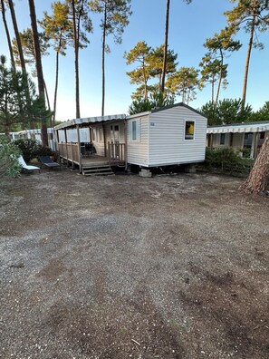 A mobile home with a porch and a small deck, surrounded by trees. - Mobile home in the heart of the Landes region (Saint-Julien-en-Born)