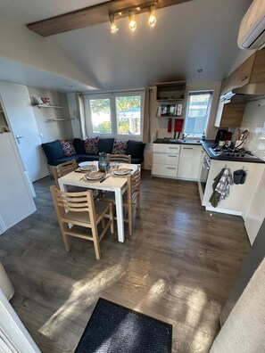 A compact kitchen with a dining area, wooden flooring, and a window providing natural light. - Mobile home in the heart of the Landes region (Saint-Julien-en-Born)