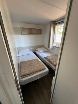 A compact room with two beds, a small shelf, and a window. - Mobile home in the heart of the Landes region (Saint-Julien-en-Born)