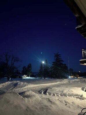 A snowy landscape at night with a streetlight and a house in the background.