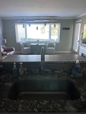 A kitchen with a granite countertop, stainless steel sink, and two white chairs.