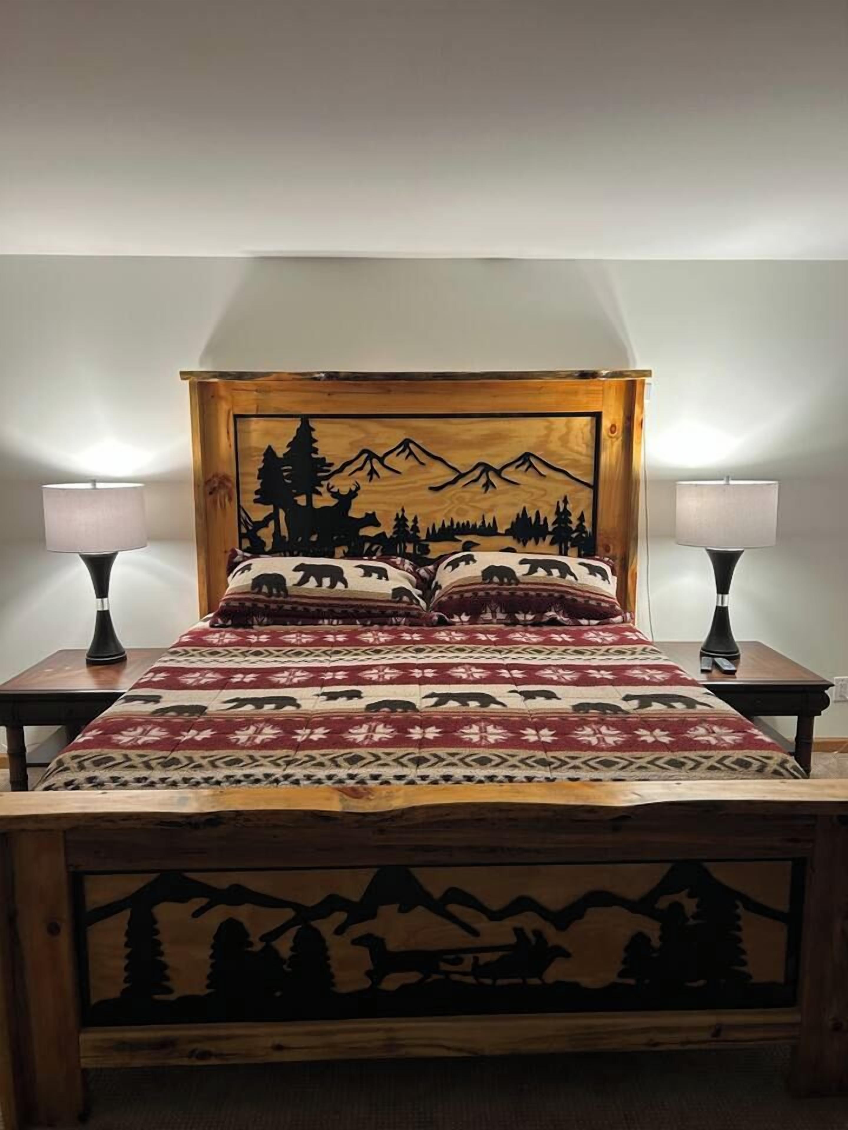 Un lit doté d’une tête de lit en bois ornée d’une silhouette représentant une montagne et une forêt, et flanqué de deux lampes de chevet.