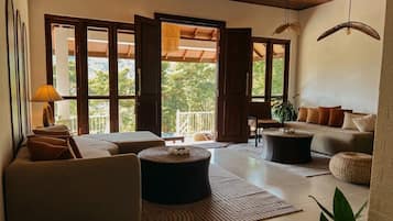 Una sala de estar moderna con sofá, reposapiés y una mesita de centro. Hay un ventanal con vistas a zonas verdes.