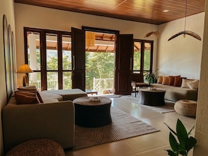 Una sala de estar moderna con sofá, reposapiés y una mesita de centro. Hay un ventanal con vistas a zonas verdes.