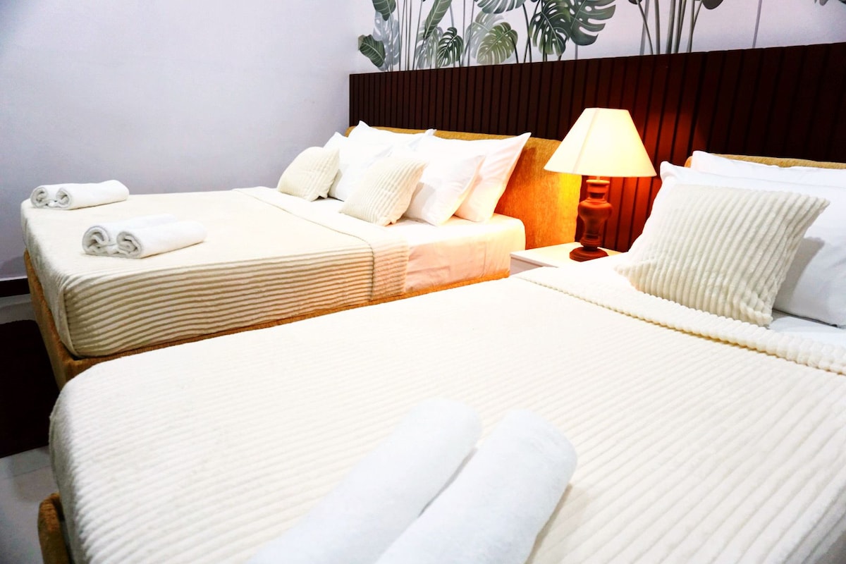 A hotel room with two beds, each with white linens and pillows, a wooden headboard, and a bedside lamp.