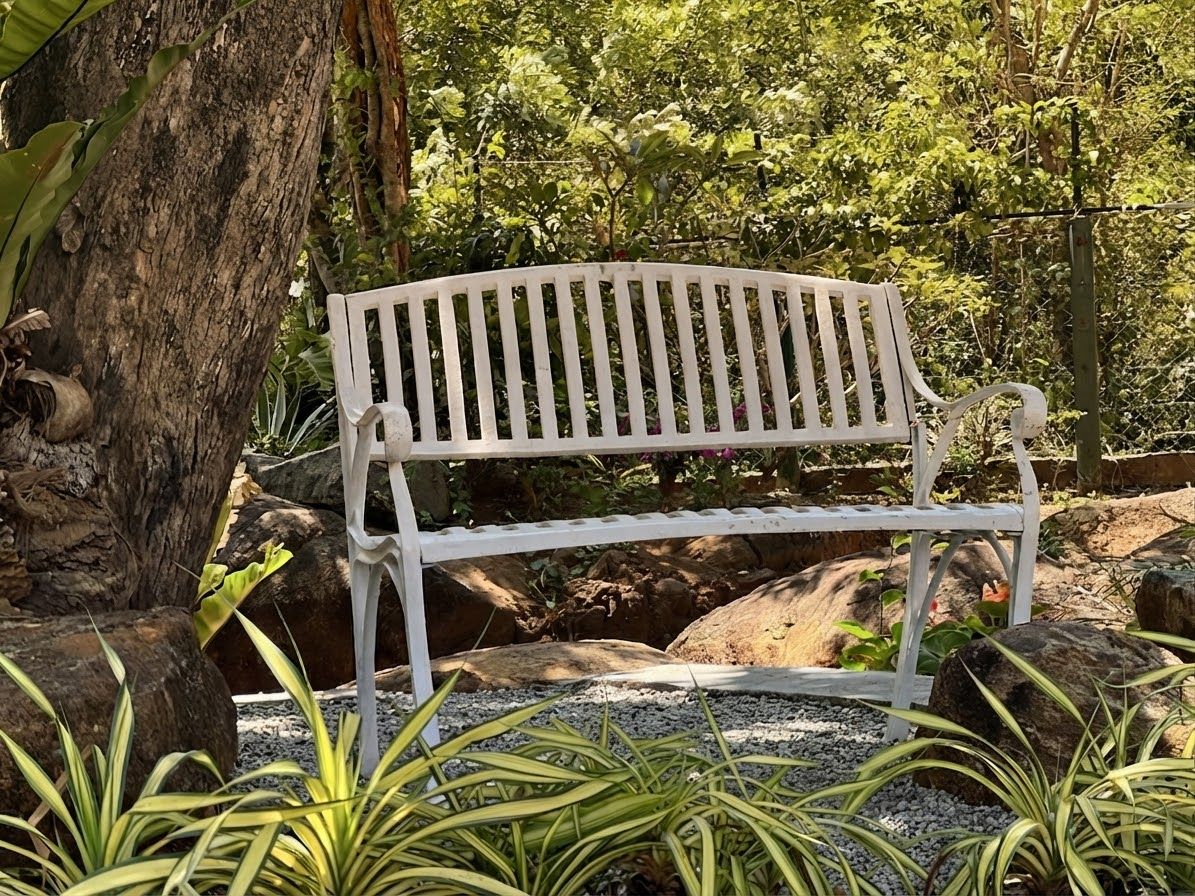 Un banco blanco en un jardín con rocas y plantas.