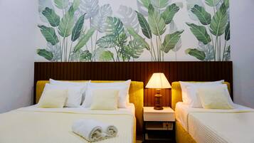 A hotel room with two beds, a nightstand with a lamp, and a wall mural of tropical leaves.