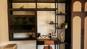 Una habitación con un mueble bajo de televisión de madera oscura, una mesita de noche de mimbre y un sillón con cojín marrón.