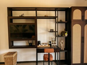 A room with a dark wooden TV stand, a wicker side table, and a brown cushioned chair. - Riverston Glade (Laggala)