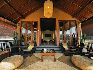 A covered outdoor seating area with a chess table, wooden chairs, and a view of the interior.
