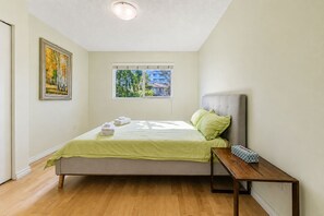 A bedroom with a bed, a window, a painting, and a bedside table. - Peaceful Westside Stay / Near Sky Train & Dining (Vancouver)