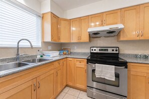 A kitchen with wooden cabinets, a stainless steel sink, a double oven, and a window with blinds. - Peaceful Westside Stay / Near Sky Train & Dining (Vancouver)