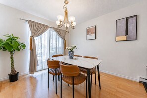 A dining area with a table, chairs, a chandelier, a potted plant, and a window with curtains. - Peaceful Westside Stay / Near Sky Train & Dining (Vancouver)
