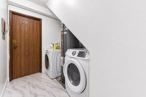 A laundry room with two washing machines, a wooden door, and a white tiled floor. - Peaceful Westside Stay / Near Sky Train & Dining (Vancouver)