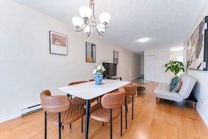 A dining area with a white table, brown chairs, a vase of flowers, and a chandelier. - Peaceful Westside Stay / Near Sky Train & Dining (Vancouver)