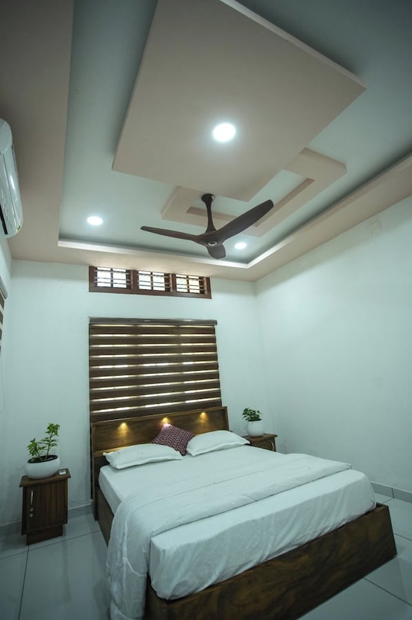 Une chambre à coucher avec un lit, des tables de chevet, un ventilateur de plafond et une fenêtre avec des stores.