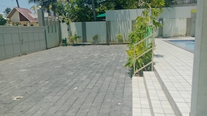 Un área exterior pavimentada con piscina, entrada protegida por un portón y un pequeño jardín.
