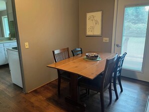 A dining area with a wooden table and chairs, a small side table with a basket, and a window with blinds. - 80-Acre Northern Michigan Lodge~Trails & Fire Pit (Wolverine)