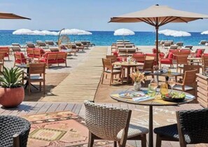 Ein Restaurant direkt am Strand mit Außenbestuhlung, Sonnenschirmen und Blick auf den Ozean.