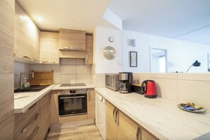 Een moderne keuken met houten kastjes, een inbouwoven, een magnetron, een koffiezetapparaat en een waterkoker.