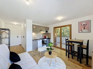 Ett modernt vardagsrum med en soffa, ett litet runt bord med en växt och en matplats med ett bord och stolar.