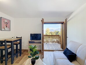 Ein Zimmer mit einem Holztisch, einer Couch, einem Fernseher und einem Balkon mit Bergblick.