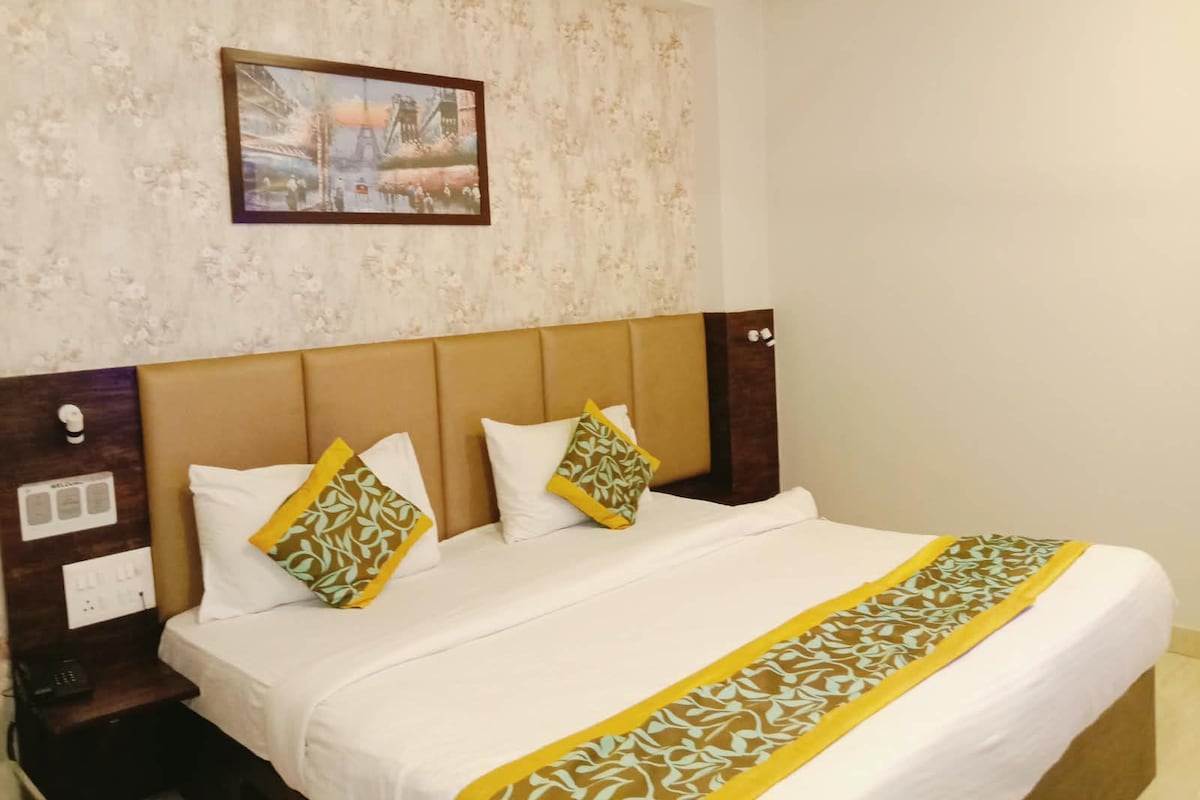 A hotel room with a bed, a nightstand, a wall-mounted painting, and a patterned bedspread.
