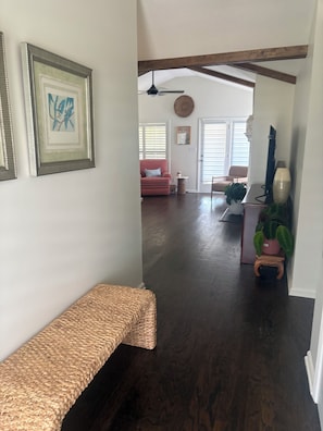 A hallway with a woven bench, a ceiling fan, and a door leading to a living room with a pink sofa and a plant. - Life on the Lake, Come on down to South GA, only three miles to the Fl. line (Lake Park)