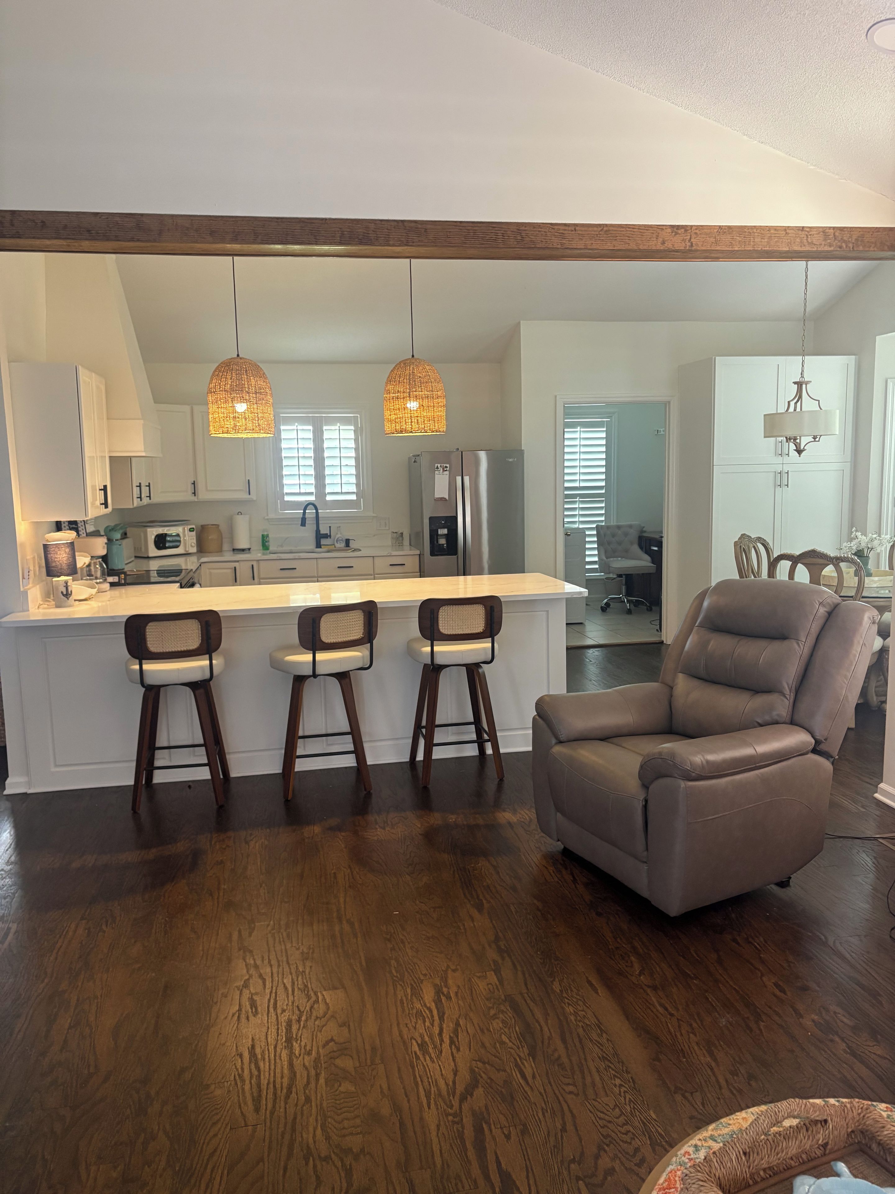 A modern kitchen with a central island, bar stools, and a leather chair.