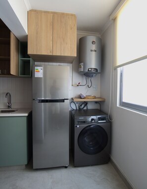 Eine kompakte Küche mit Edelstahl-Kühlschrank, Waschmaschine und eingebautem Durchlauferhitzer.