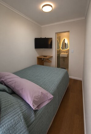 Ein Schlafzimmer mit einem Bett, einem an der Wand montierten Fernseher, einem Nachttisch und einem Spiegel.